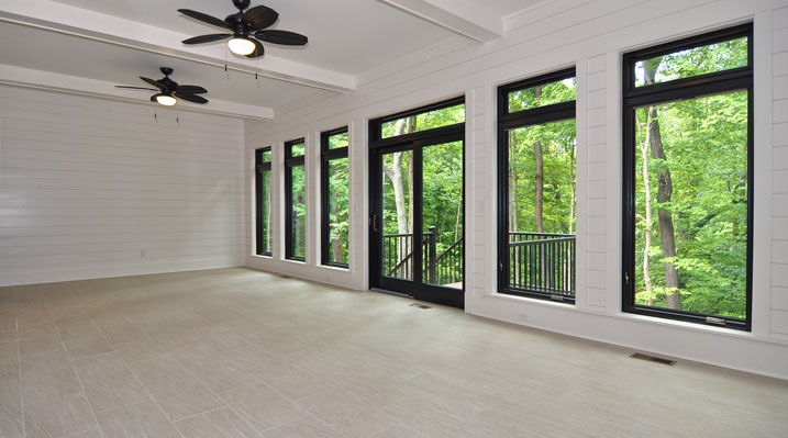 ICH Lithopolis Ohio residence custom build large sun room with white walls and black trim, 2 black ceiling fans and large floor to ceiling windows facing the back yard