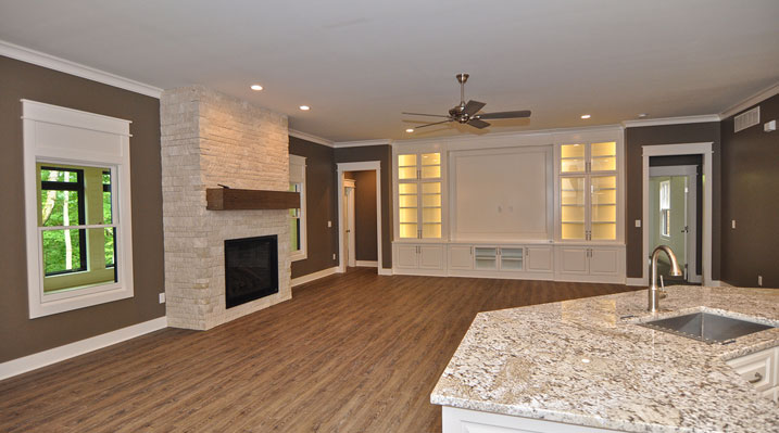 ICH Lithopolis Ohio residence custom build another view of the large living area showcasing the wooden floors, white stone fireplace and custom-built white painted entertainment unit along the far wall featuring upper cabinets with glass-front mullion doors, integrated lighting, and lower storage