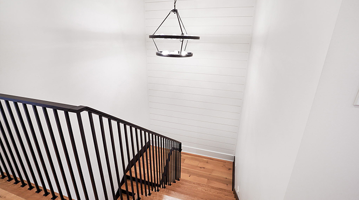 ICH Builders Canal Winchester Ohio residence custom build view looking down wooden staircase and iron railing with hanging black iron chandelier over the landing