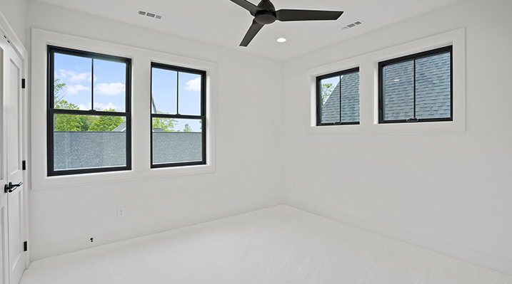 ICH Builders Canal Winchester Ohio residence custom build another smaller corner bedroom with white walls with 2 windows on each wall and a hanging 3 blade modern black ceiling fan above