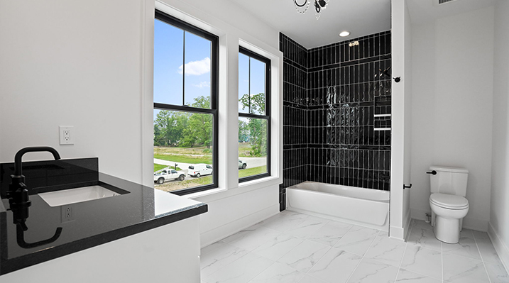 ICH Builders Canal Winchester Ohio residence custom build white walled bathroom with white vanity and black countertop and black fixtures in foreground and white bathtub with black tiling in background