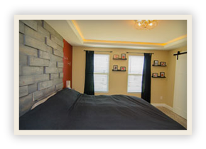 thumbnail image of Iulianelli Custom Homes Richwood Model bedroom with dimensional, textured gray brick accent wall behind the bed and a recessed tray ceiling with warm hidden lighting