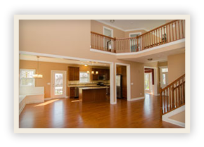 thumbnail image of Iulianelli Custom Homes Oakland Model showing open-concept living area with hardwood floors, a kitchen with a center island, and a staircase leading to a second-floor balcony. 